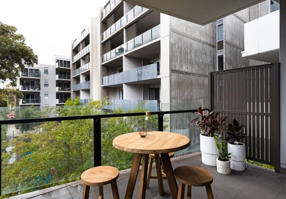 a balcony with a table and three stools in front of an apartment building