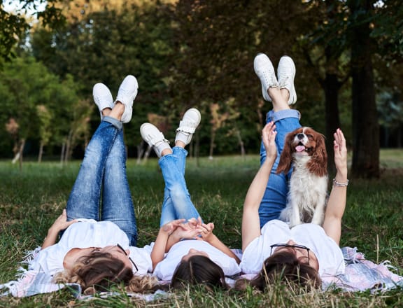 three girls laying in the grass with their feet up in the air and a dog