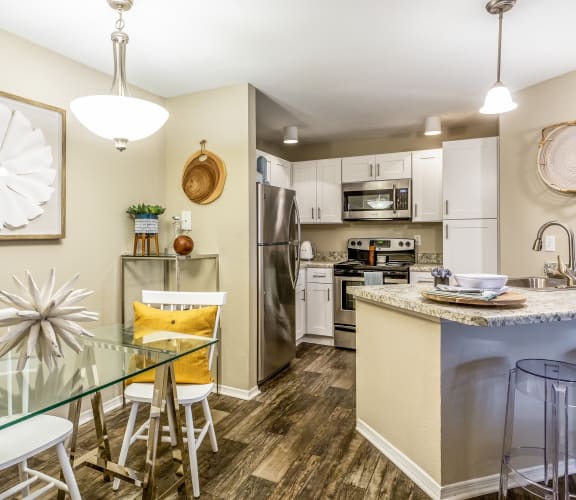 a dining area with a glass table and chairs and a kitchen with stainless steel appliances at Fusion Apartments, Orlando, FL 32818