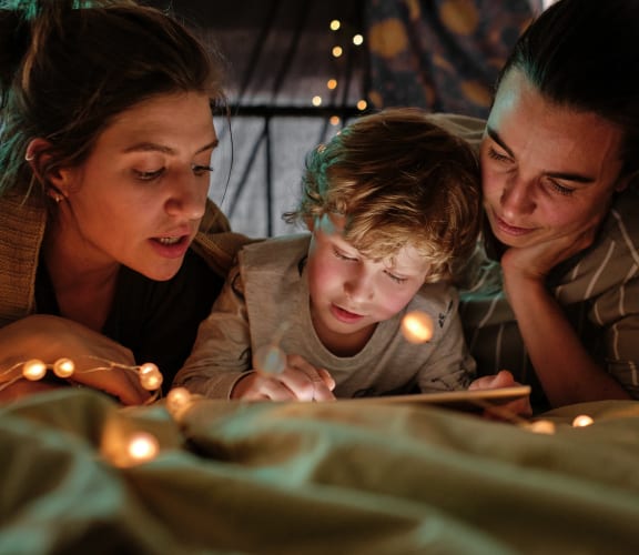 a family lying on a bed reading a book with christmas lights around them