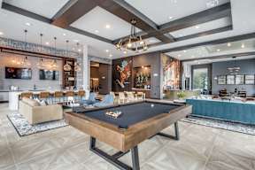 A pool table is in the middle of a room with a high ceiling and a bar area.