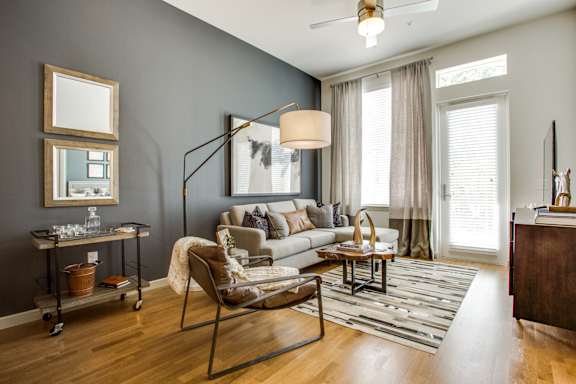 A living room with a grey couch, a wooden floor, and a ceiling fan.