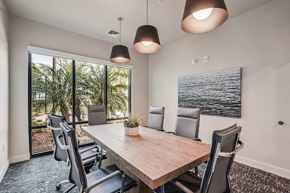 A conference room with a long table and chairs, a plant, and a painting on the wall at The Stadler Luxury Apartments, Bradenton, 34210