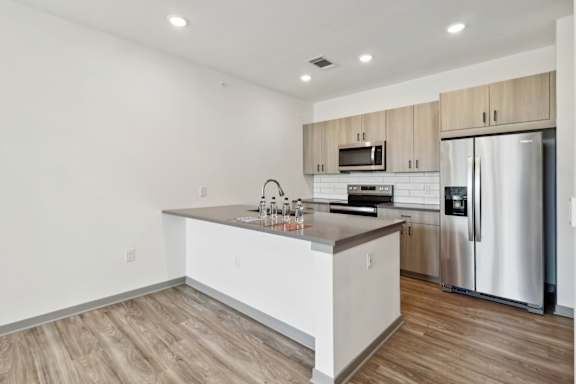 a kitchen with a large island and a stainless steel refrigerator at The Depot Luxury Apartment Homes, Raymore, 64083