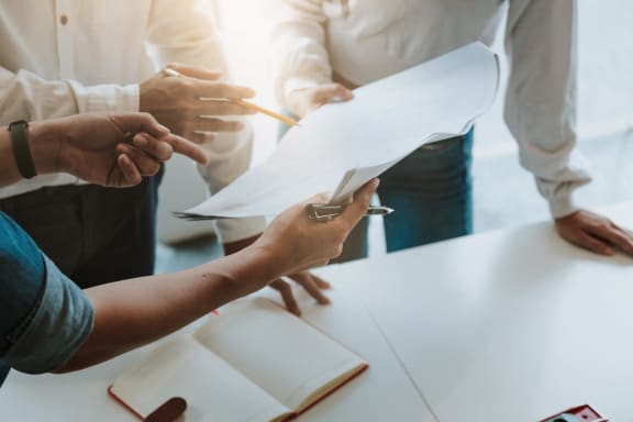 a group of people standing around a table discussing paper