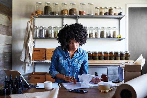A woman with curly hair is working at a desk with various items on it.