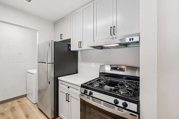 A kitchen with a black fridge, stainless steel oven and white cabinets.