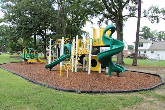 A playground with a green slide and yellow safety bars.