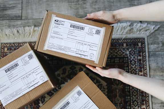 Three boxes with shipping labels are being held by a person.