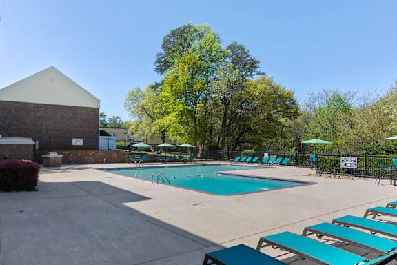 a swimming pool with chaise lounge chairs and umbrellas in front of a at Lakecrest Apartments, PRG Real Estate Management, Greenville, South Carolina