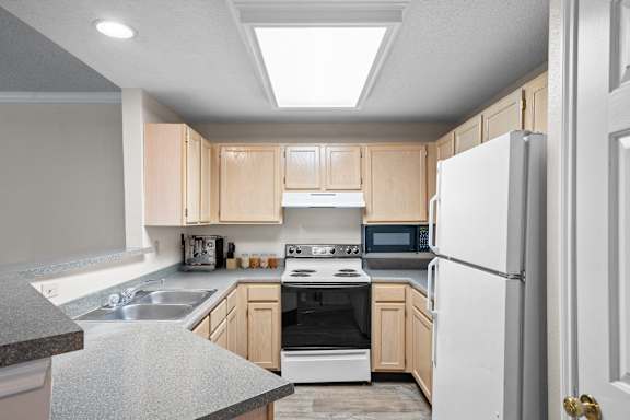 A kitchen with wooden cabinets and white appliances.at The Claremont Apartment Homes, Overland Park