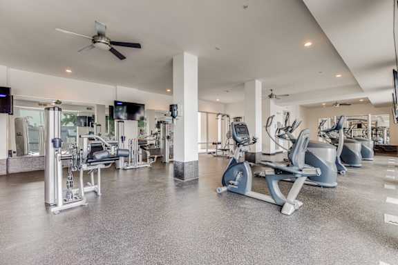 a gym with cardio machines and a ceiling fan