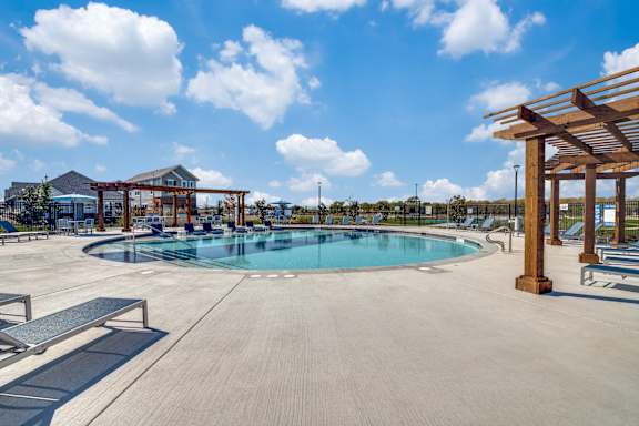 A large outdoor swimming pool surrounded by a wooden pergola and benches.