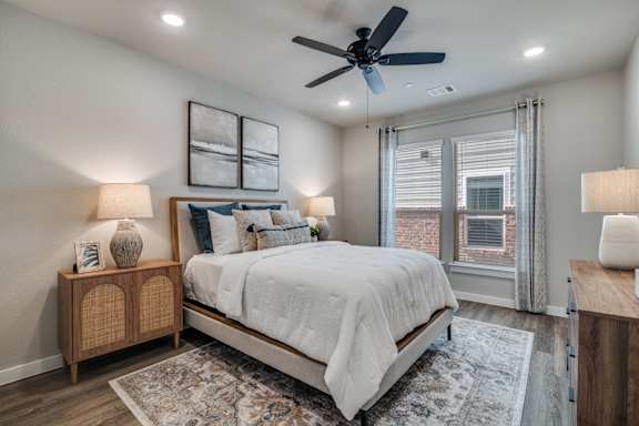 A bedroom with a bed, two lamps, and a ceiling fan.