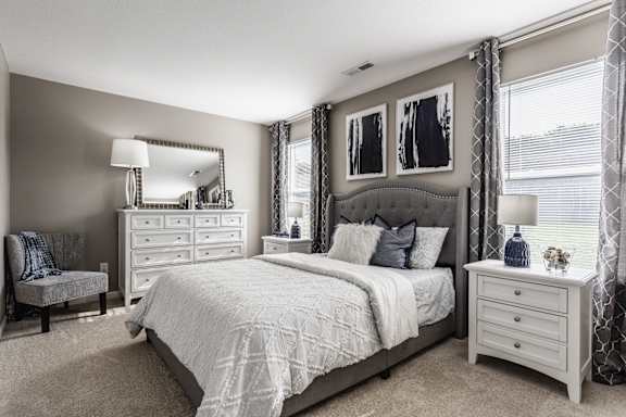 A bedroom with a large bed, a nightstand, and a window with white curtains.