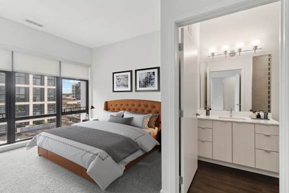 A bedroom with a large bed and a bathroom with a vanity and mirror.