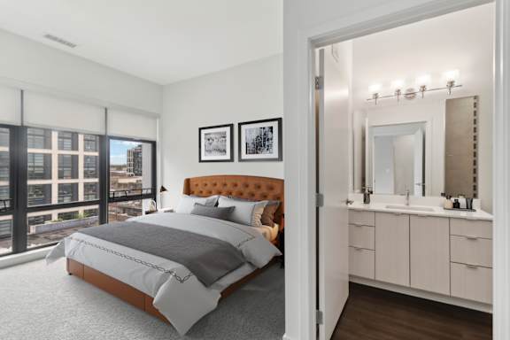 A bedroom with a large bed and a bathroom with a vanity and mirror.