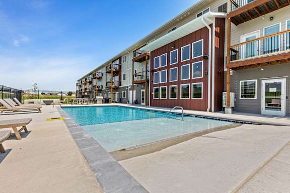 A swimming pool is surrounded by a concrete patio and a building with a red and white exterior.