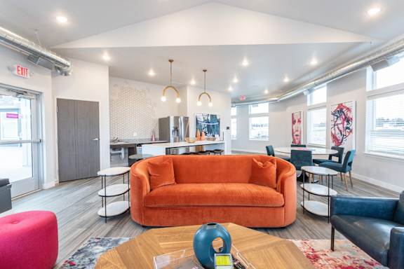 A brightly lit room with a large orange couch and a coffee table in the center.