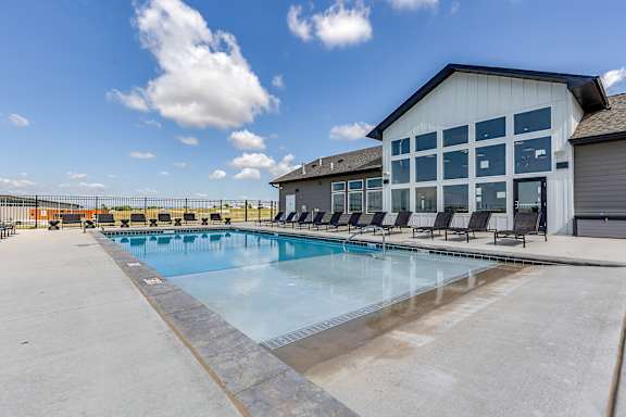 A large outdoor swimming pool with lounge chairs and a building in the background.