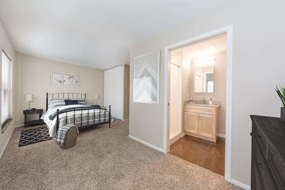 A bedroom with a bed, nightstand, and a small bathroom with a sink.