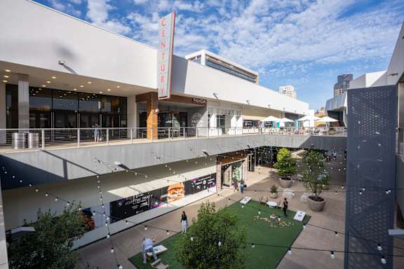 A view of a shopping mall with a green lawn and people walking around.