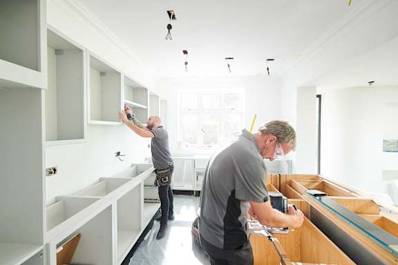 two men working in a kitchen with a cabinet installation