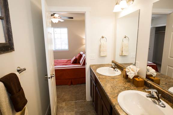 Image of bathroom with master bedroom containing two sinks, two mirrors, and towel rack
