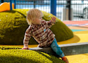 Thumbnail 5 of 7 - A young child in a plaid shirt and blue jeans is playing on a playground.