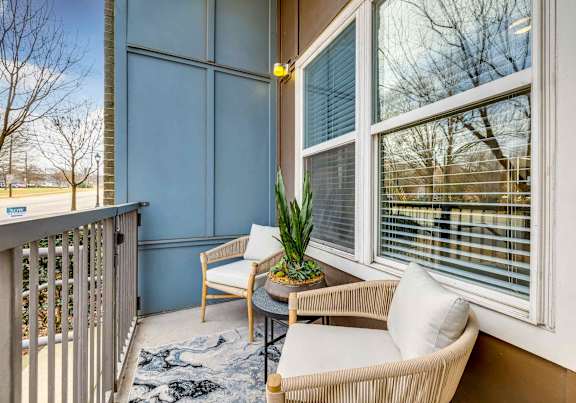 A balcony with a table, chairs, and a potted plant.