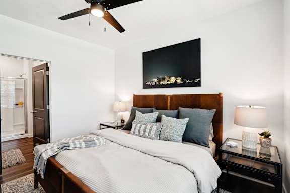 A bedroom with a large bed, a ceiling fan, and a flat-screen TV mounted above the bed.