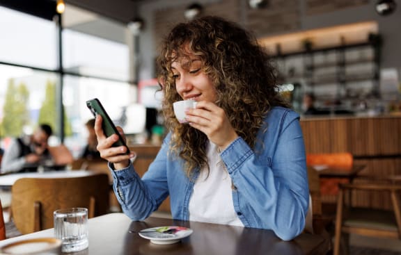 a woman sitting at a table drinking coffee and looking at her cell phone at Sunset Barrington Gardens, Los Angeles, CA