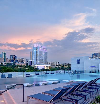 A rooftop pool area with lounge chairs and a city skyline in the background.