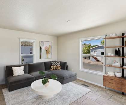 A living room with a grey couch, a white coffee table, and a large window.