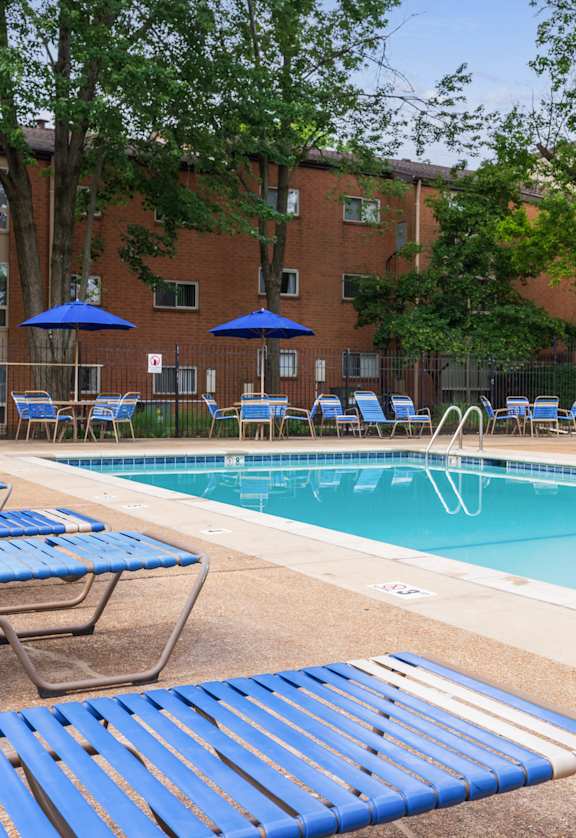 a swimming pool with chaise lounge chairs and umbrellas in front of a brick building