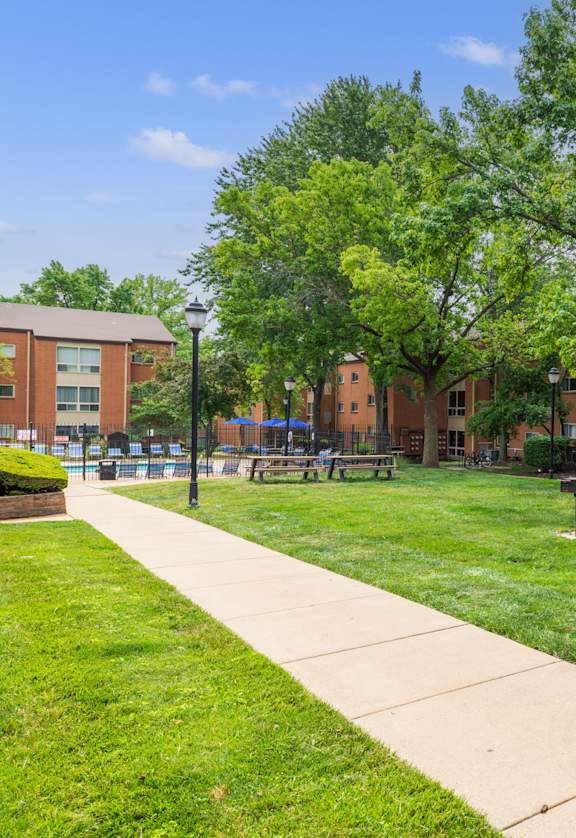 a grassy area with trees and a walkway in front of a brick building