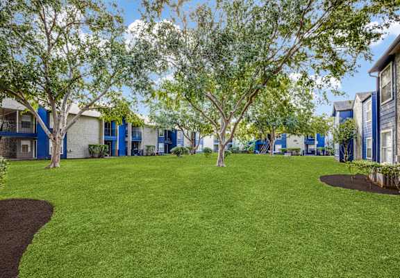A grassy area with trees and houses in the background.
