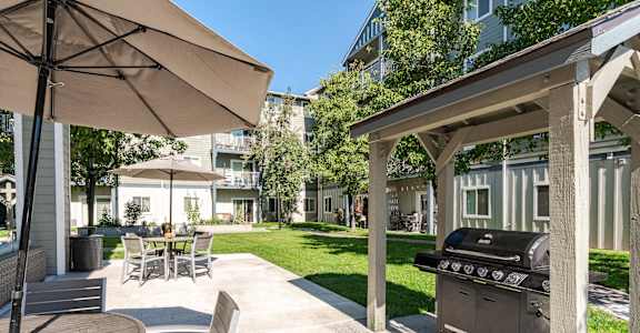 A patio with a grill and chairs under an umbrella.