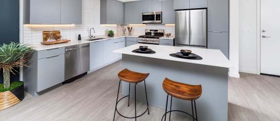 A modern kitchen with a bar stool and a hanging light fixture.