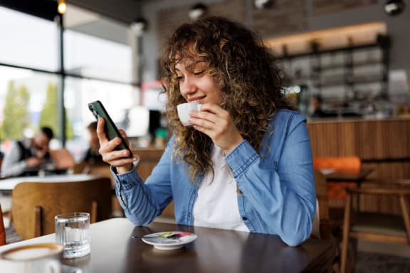 a woman sitting at a table drinking coffee and looking at her cell phone at Pleasanton Glen Apartments, Pleasanton, CA, 94566