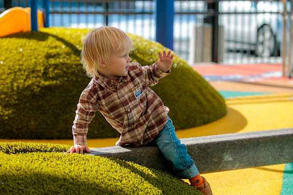 A young child in a plaid shirt and blue jeans is playing on a playground.