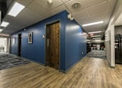 Thumbnail 6 of 14 - a hallway with a blue wall and wooden floors and doors at 100 South Apartments, Buffalo, NY 14202