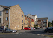 Thumbnail 2 of 5 - a city street with cars parked in front of brick apartment buildings