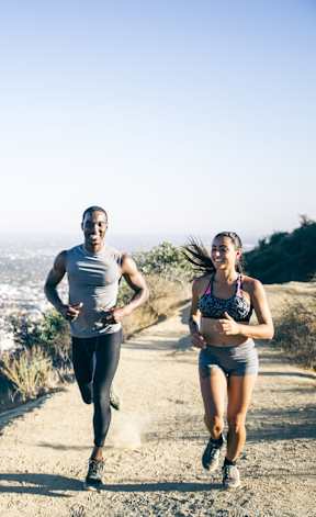 Two people running on a trail with a cityscape in the background.