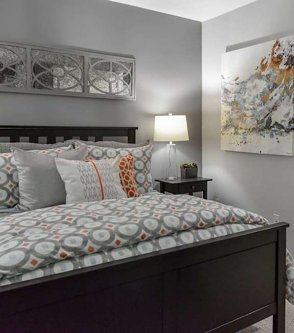 A bedroom with a bed, nightstand, lamp, and artwork on the wall.