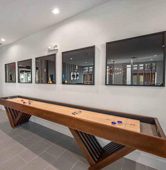 A long wooden table with blue coasters is in the middle of a room with mirrors on the wall.