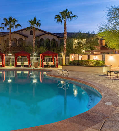 A swimming pool surrounded by palm trees and red umbrellas.