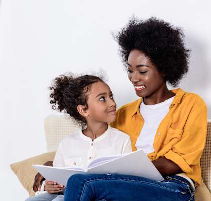 a mother and daughter sitting on a couch reading a book