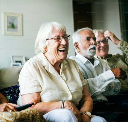 A group of elderly people are sitting on a couch and laughing together.