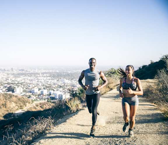 Two people running on a trail with a cityscape in the background.